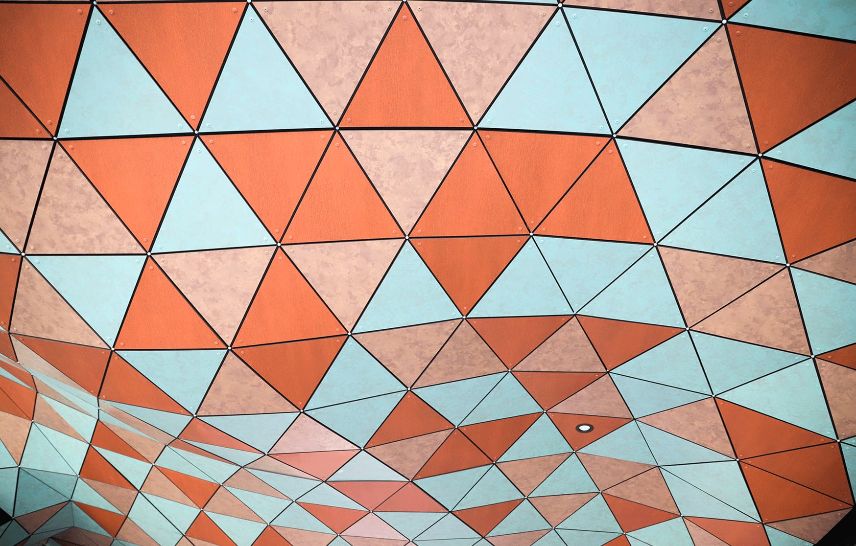 Looking up at Anemoi's billowing Trespa Meteon soffit, its copper and pale blue triangles rippling like wind over Fremantle