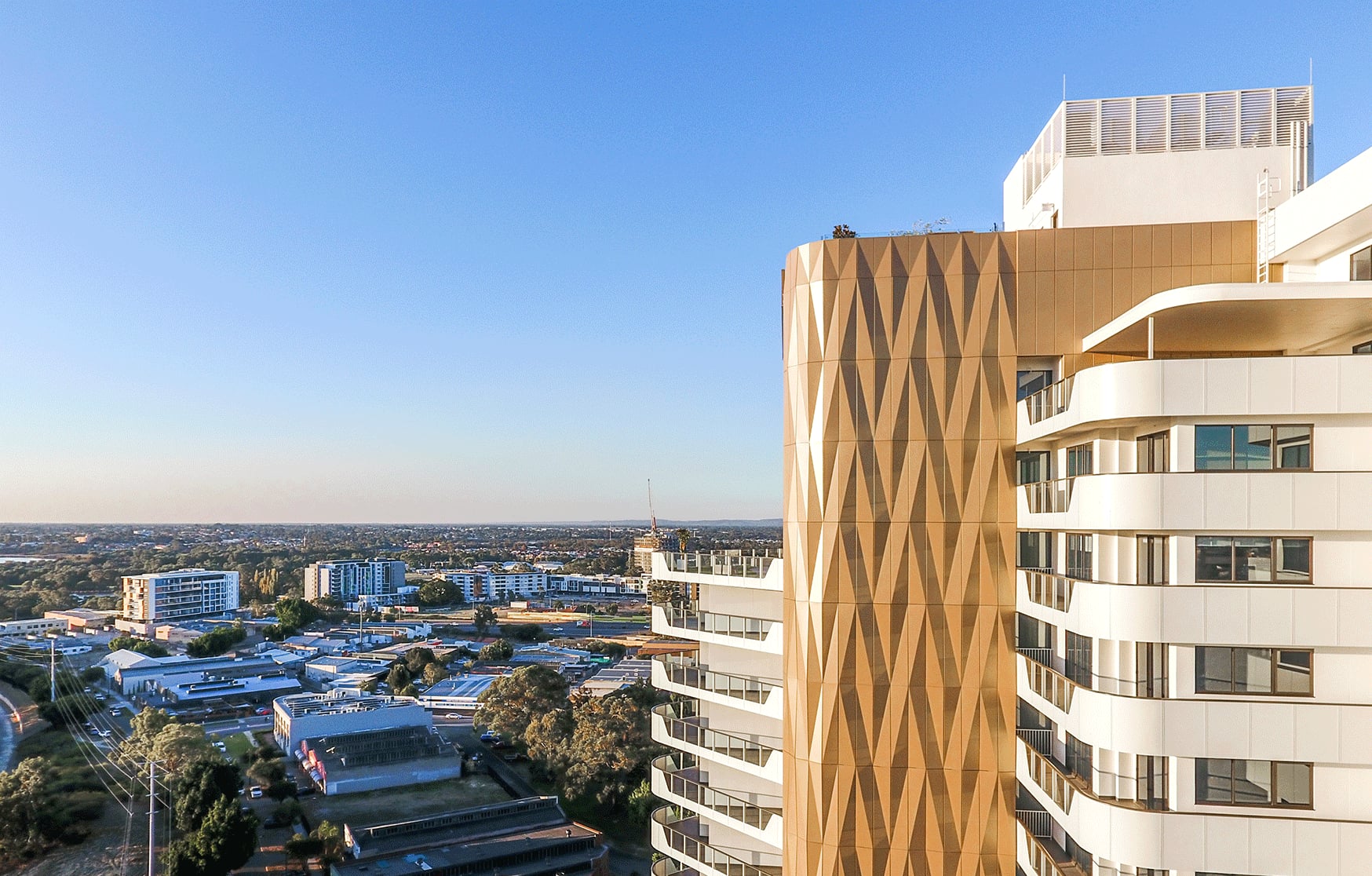 Drone view of Folding Light crowning The Crest tower in Burswood, gold folded aluminium catching the late sun.