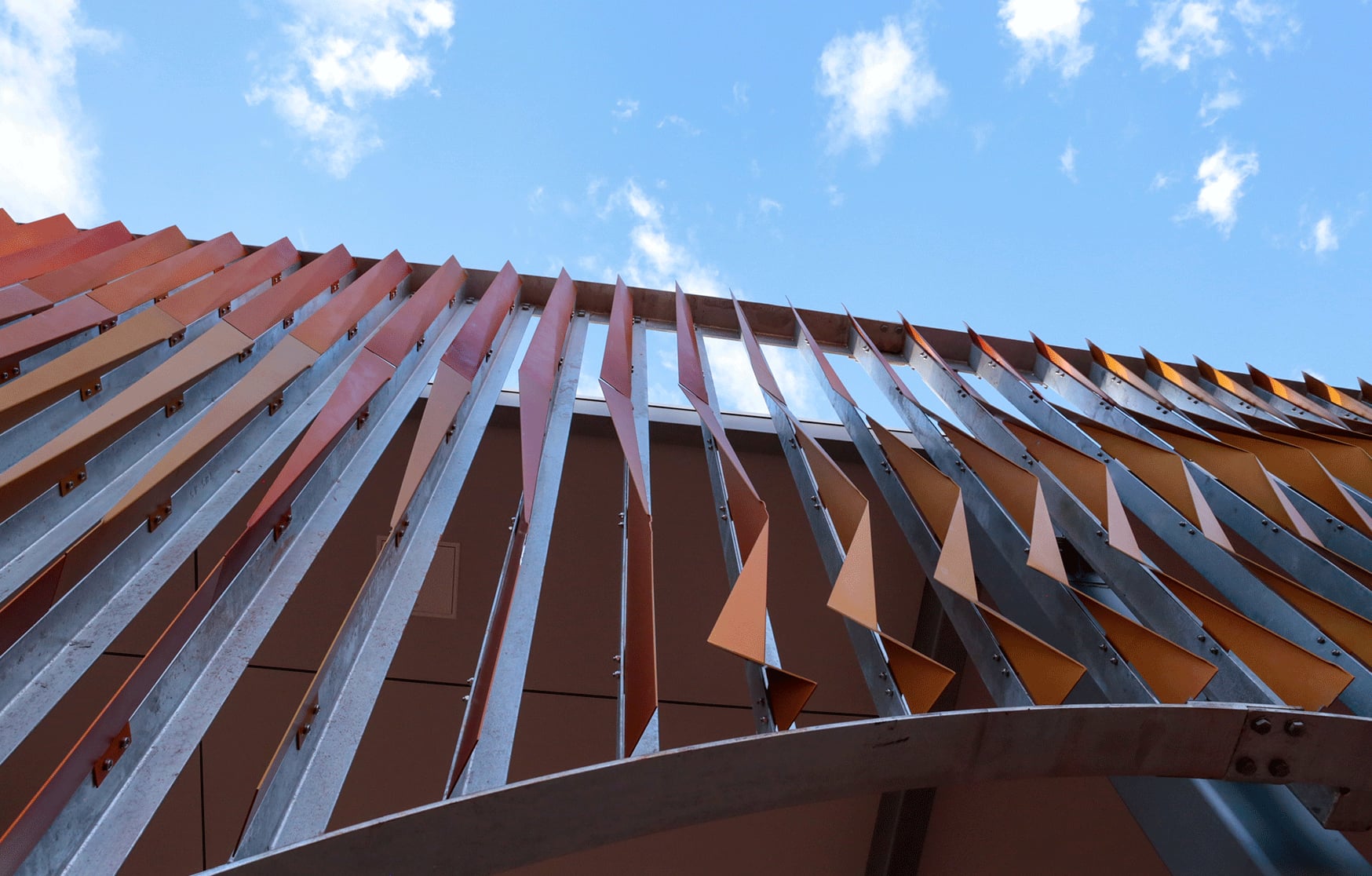 Looking up at the orange folded aluminium fins of Pleated Histories rippling against a Broome sky.